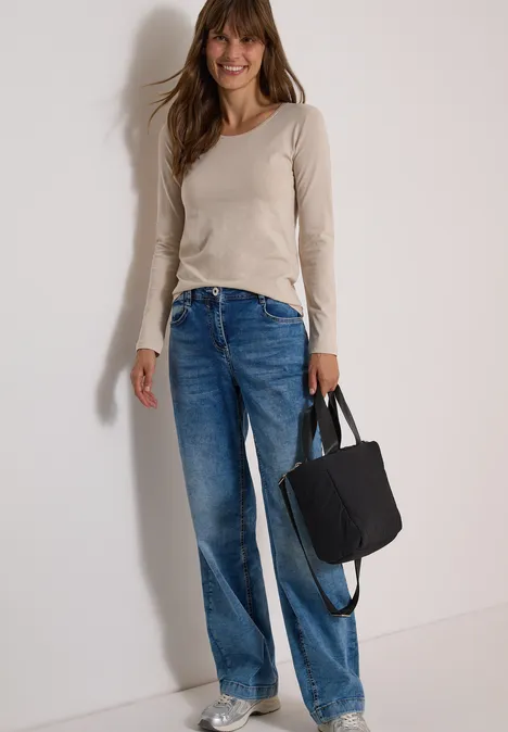 Basic Shirt mit Rundhals im 2er-Pack cashmere beige/black Frau trägt Jeans, beiges Langarmshirt, schwarze Tasche, lächelt vor neutralem Hintergrund.
