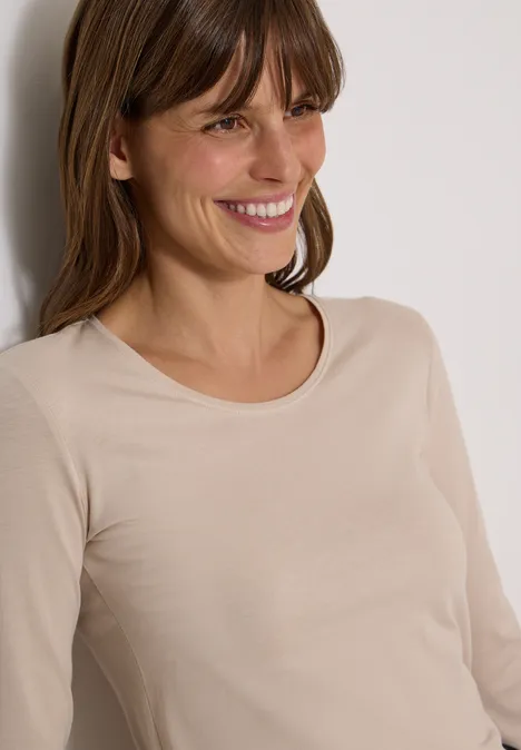Basic Shirt mit Rundhals im 2er-Pack cashmere beige/black Eine lächelnde Frau lehnt an einer Wand und trägt ein schlichtes beigefarbenes Langarmshirt.