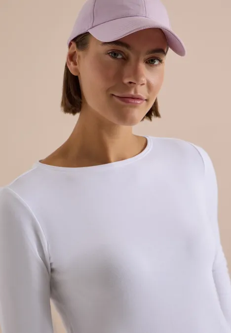 Porträt einer jungen Frau mit weißem Shirt und fliederfarbener Cap vor neutralem Hintergrund.