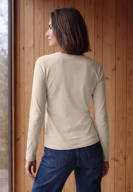 Langarm Shirt in Unifarbe mit V-Neck cashmere beige Frau in langärmeligem beigem Shirt und Jeans, Rückansicht vor einer Holzverkleidung.