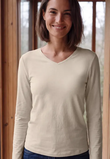 Langarm Shirt in Unifarbe mit V-Neck cashmere beige Eine lächelnde Frau vor einem Fenster, trägt cremefarbenes, langärmliges V-Neck-Shirt.