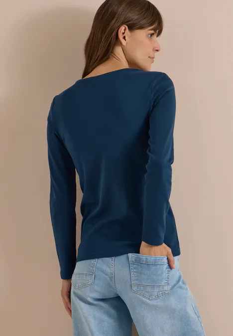 Langarm Shirt in Unifarbe mit V-Neck moonlight blue Frau von hinten in dunkelblauem Langarmshirt und hellen Jeans vor beigem Hintergrund.