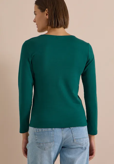 Langarm Shirt in Unifarbe mit V-Neck dark fir green Rückenansicht einer Frau in grünem Langarmshirt und blauen Jeans.