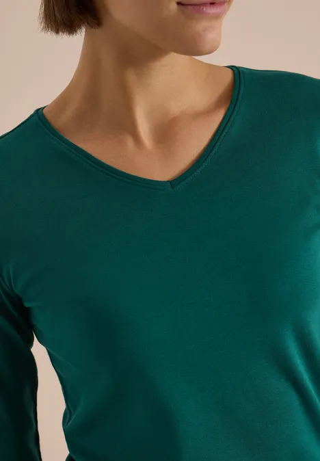 Langarm Shirt in Unifarbe mit V-Neck dark fir green Frau mit grünem V-Ausschnitt-Shirt, nur Schultern und unterer Teil des Gesichts sichtbar.