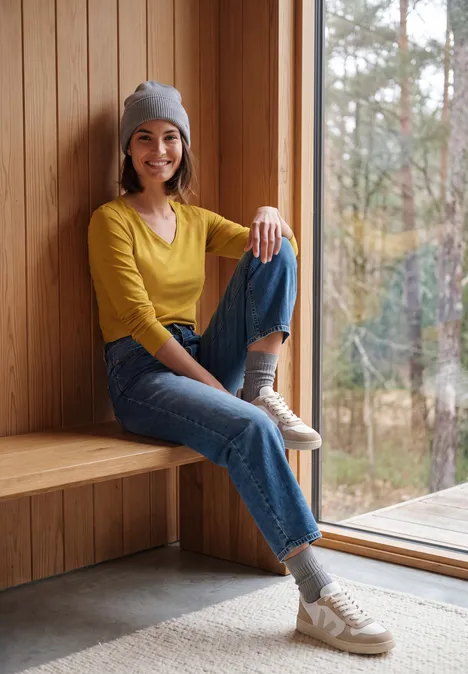 Langarm Shirt in Unifarbe mit V-Neck golden honey Junge Frau in Mütze und Jeans sitzt entspannt am Fenster mit Blick ins Grüne.