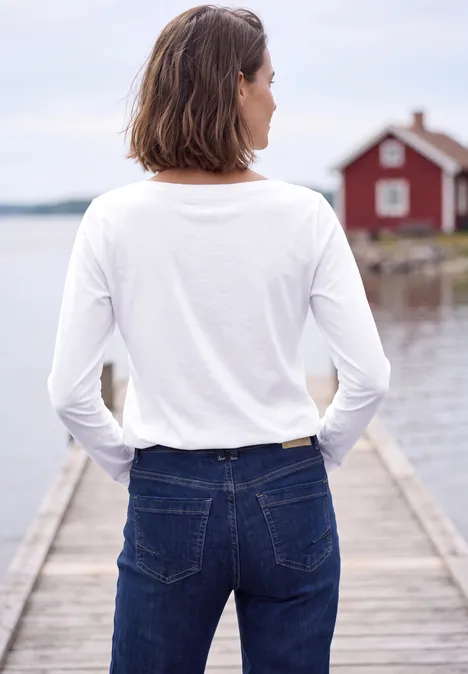 Langarm Shirt mit U-Boot-Ausschnitt White Person mit weißem Langarmshirt und Jeans steht auf Holzsteg, Blick aufs Wasser und rotes Haus.