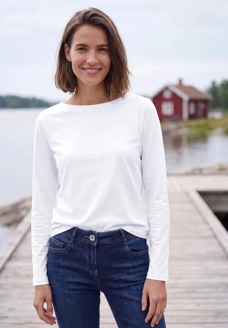 Langarm Shirt mit U-Boot-Ausschnitt White Junge Frau in weißem Shirt und Jeans steht lächelnd auf einem Steg am See mit rotem Bootshaus.
