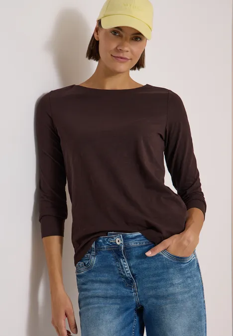 Langarm Shirt mit U-Boot-Ausschnitt truffle brown Frau in gelber Kappe, braunem Langarmshirt und Jeans, eine Hand in der Tasche, entspannt stehend.