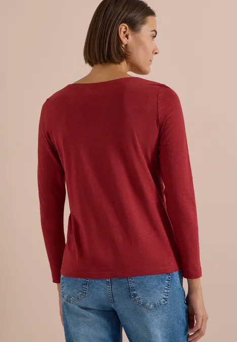 Langarm Shirt mit U-Boot-Ausschnitt russet red Frau von hinten mit rotem Pullover und Jeans vor unauffälligem Hintergrund.