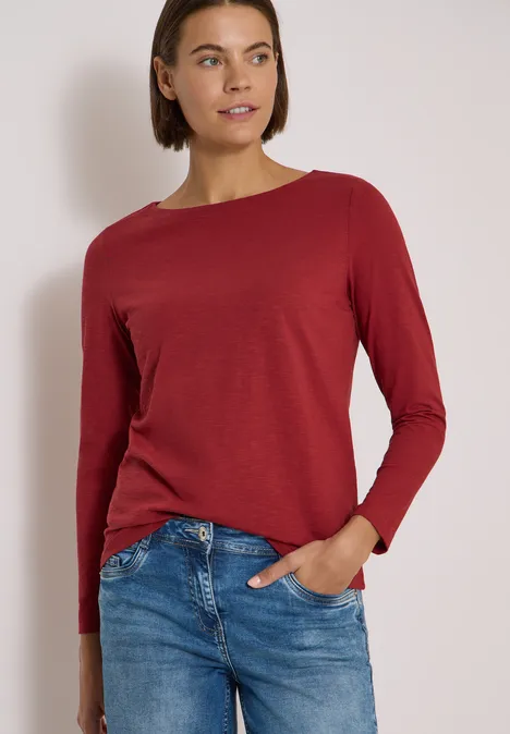 Langarm Shirt mit U-Boot-Ausschnitt russet red Frau in rotem Langarmshirt und blauen Jeans vor neutralem Hintergrund.