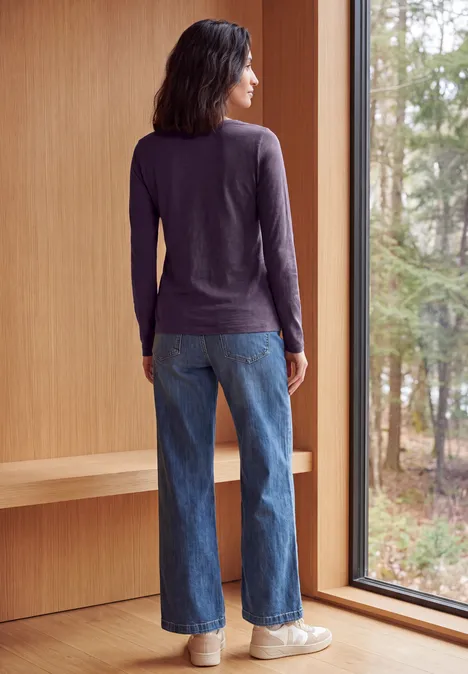 Langarm Shirt mit U-Boot-Ausschnitt lilac shadow Rückansicht einer Person in Jeans und langärmeligem Shirt, die an einem Fenster steht und in den Wald blickt.
