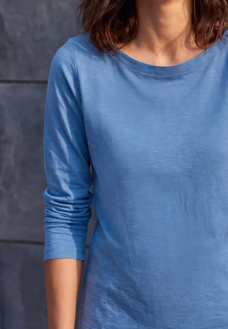 Person trägt blaues Langarmshirt vor dunklem Hintergrund.