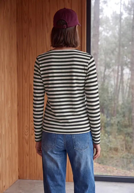 Langarm Shirt mit Boat Neck und Streifen Black Rückansicht einer Person in gestreiftem Pullover, Jeans und Kappe, die in einem Holzraum auf einen nebligen Wald blickt.