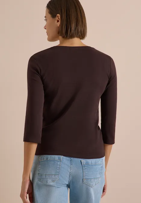 3/4-Arm Shirt in Unifarbe mit V-Neck truffle brown Eine Frau steht mit dem Rücken zur Kamera, trägt ein dunkelbraunes 3/4-Armshirt und blaue Jeans.