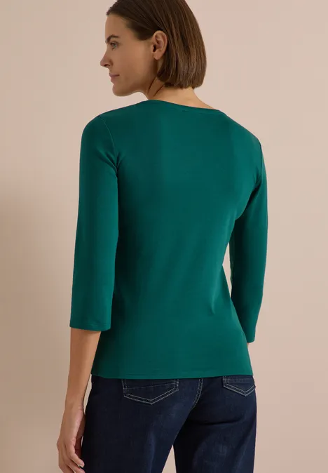 3/4-Arm Shirt in Unifarbe mit V-Neck dark fir green Frau von hinten in grünem 3/4-Arm-Pullover und Jeans vor beigem Hintergrund.