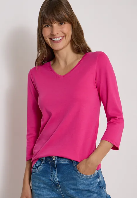 3/4-Arm Shirt in Unifarbe mit V-Neck pink flash Junge Frau in pinkem V-Ausschnittshirt und blauen Jeans, lächelt vor weißem Hintergrund.