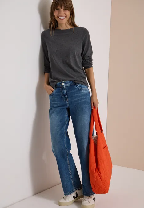 Langarm Shirt mit U-Boot-Ausschnitt black melange Junge Frau lehnt an einer Wand, trägt graues Shirt, blaue Jeans und hält eine rote Einkaufstasche.