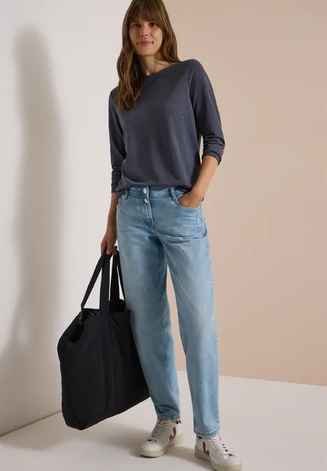 Vrouw met donkerblauwe trui, lichte jeans en witte sneakers, met een grote zwarte tas.