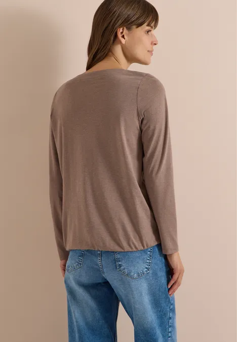Vrouw van achteren in een bruin shirt met lange mouwen en een blauwe spijkerbroek voor een beige achtergrond.