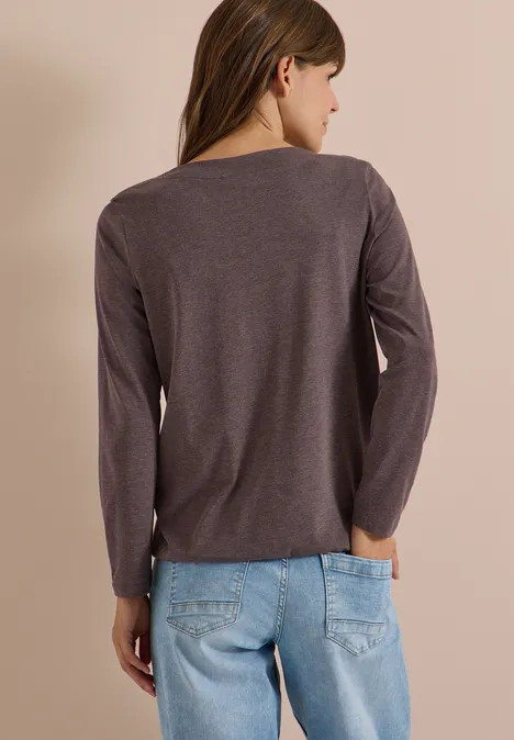 Femme vue de dos portant un tee-shirt à manches longues gris et un jean bleu clair sur fond beige.