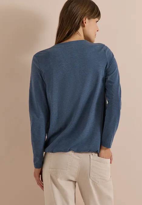 Langarm Shirt mit U-Boot-Ausschnitt moonlight blue melange Eine Frau steht mit dem Rücken zur Kamera und trägt ein blaues Langarmshirt und helle Hose.