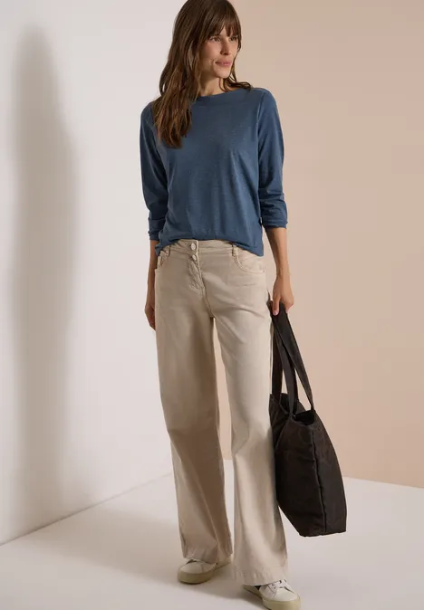 Langarm Shirt mit U-Boot-Ausschnitt moonlight blue melange Eine Frau trägt ein blaues Langarmshirt, beigefarbene weite Jeans, weiße Sneaker und eine schwarze Tasche.