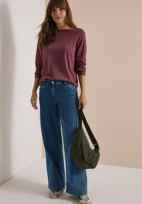 Langarm Shirt mit U-Boot-Ausschnitt red wine melange Frau in lila Langarmshirt und weiten Jeans steht vor hellem Hintergrund, trägt eine grüne Umhängetasche.