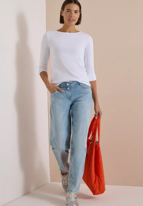 Langarm Shirt mit U-Boot-Ausschnitt White Frau in weißem Langarmshirt, weiten Jeans und Sandalen trägt orangefarbene Stofftasche vor schlichtem Hintergrund.