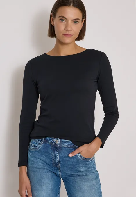 Langarm Shirt mit U-Boot-Ausschnitt Black Frau in schwarzem Langarmshirt und blauen Jeans vor neutralem Hintergrund, Hand in Tasche.