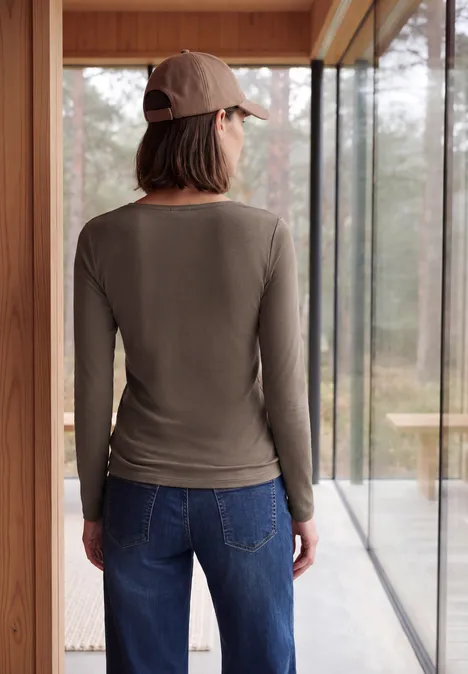 Langarm Shirt mit U-Boot-Ausschnitt urban taupe Frau von hinten in lässigem Langarmshirt, Jeans und Baseballcap, stehend vor großem Fenster mit Waldblick.