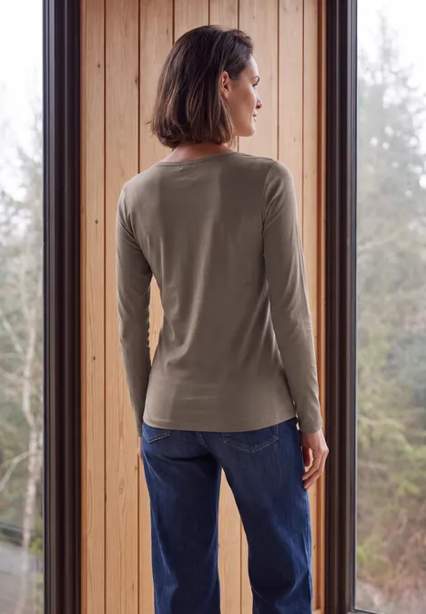 Langarm Shirt mit U-Boot-Ausschnitt urban taupe Eine Frau steht vor einem Fenster, Rückenansicht trägt ein olivgrünes Langarmshirt und blaue Jeans.