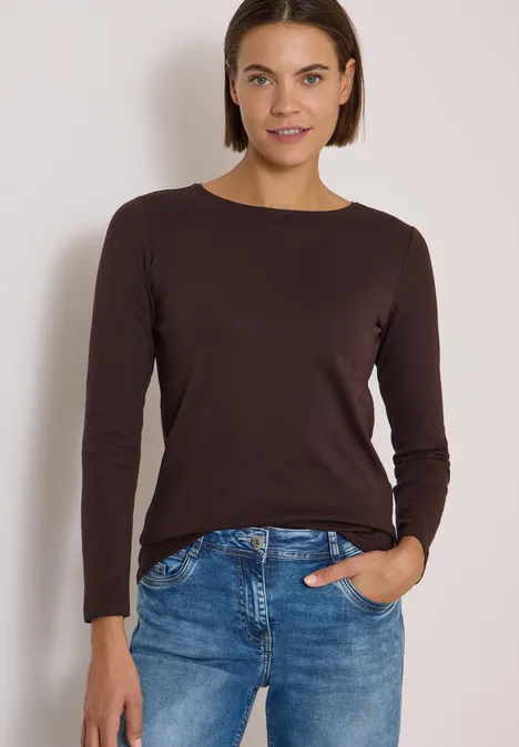 Langarm Shirt mit U-Boot-Ausschnitt truffle brown Frau mit braunem Langarmshirt und blauen Jeans, eine Hand in der Tasche, lächelnd vor neutralem Hintergrund.