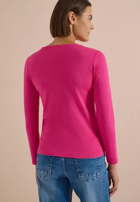 Langarm Shirt mit U-Boot-Ausschnitt pink flash Eine Frau von hinten in pinkem Langarmshirt und blauen Jeans vor beigem Hintergrund.
