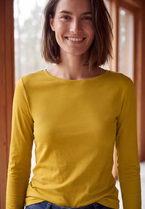 Langarm Shirt mit U-Boot-Ausschnitt golden honey Eine lächelnde Frau in gelbem Langarmshirt vor einem Fenster.