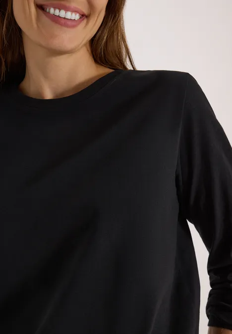 Une personne porte un t-shirt noir à manches trois-quarts et col rond, souriante.