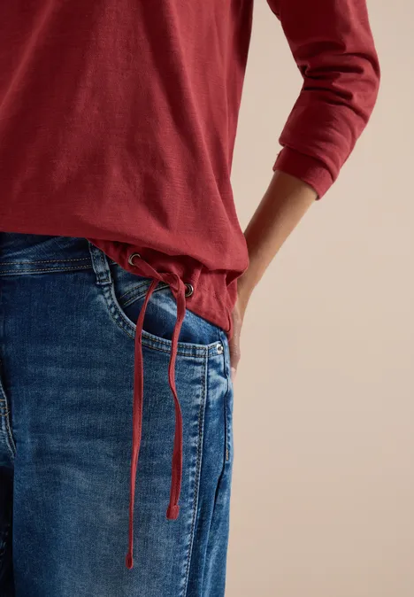 Langarm Shirt mit Rundhals und Tunnelzug russet red Person trägt rotes Langarmshirt und blaue Jeans mit Kordelzug, Hand in Tasche vor beigem Hintergrund.