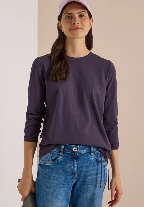 Langarm Shirt mit Rundhals und Tunnelzug lilac shadow Frau in lila Langarmshirt, blauer Jeans und Cap vor neutralem Hintergrund.