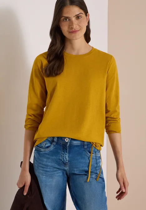 Langarm Shirt mit Rundhals und Tunnelzug golden honey Frau in gelbem Pullover mit langen Ärmeln und blauer Jeans, hält eine schwarze Tasche.