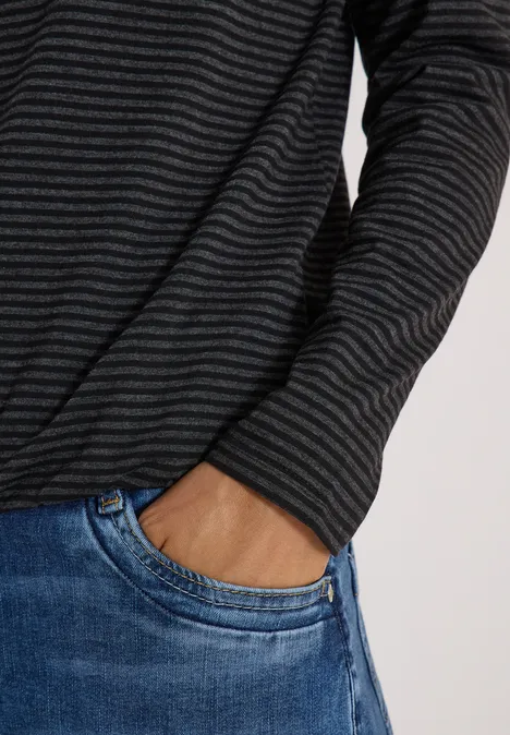 Personne portant un pull gris foncé à fines rayures, main dans la poche d’un jean bleu.
