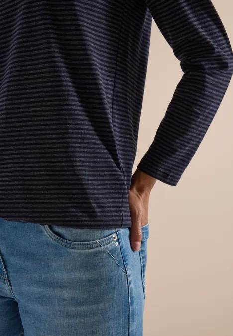 Vue partielle d'une personne en t-shirt à rayures et jean, main dans la poche.