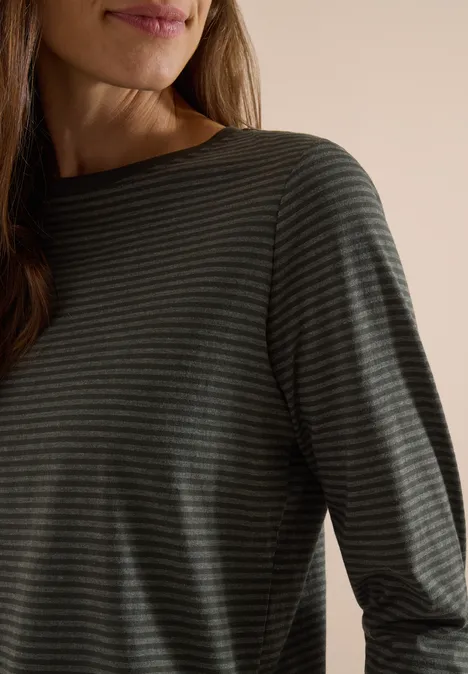 Gros plan sur une personne portant un t-shirt à manches longues à fines rayures sombre sur fond neutre.