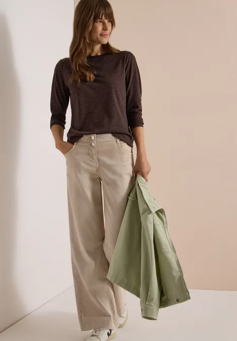 Langarm Shirt mit Boat Neck und Streifen truffle brown Eine Frau in dunkelbraunem Langarmshirt, hellen weiten Hosen und grüner Jacke in der Hand.