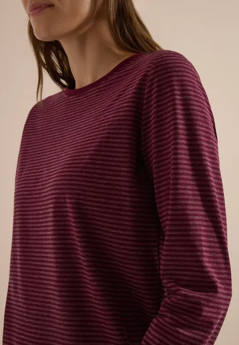 Femme en pull à manches longues bordeaux à rayures noires, fond neutre.