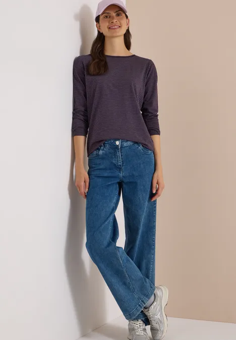 Langarm Shirt mit Boat Neck und Streifen lilac shadow Frau in lila 3/4-Arm-Shirt, blauen Jeans, weißen Sneakern und rosa Cap lehnt an heller Wand.