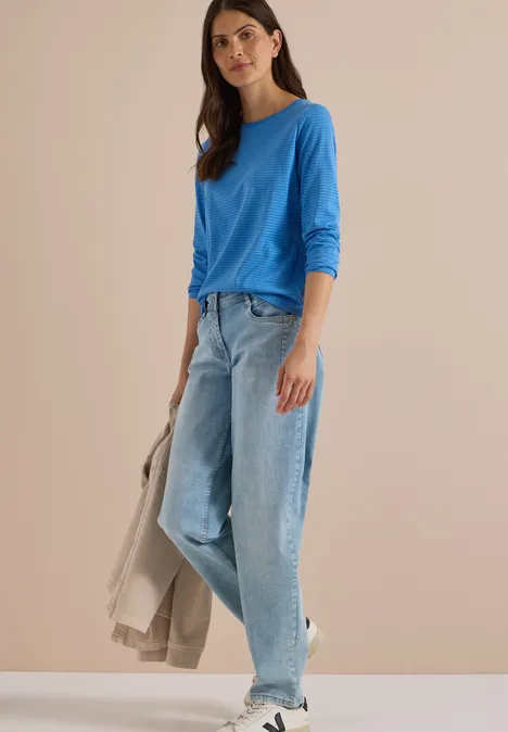 Langarm Shirt mit Boat Neck und Streifen north blue Frau in blauem Langarmshirt, weiten Jeans und Sneakers vor neutralem Hintergrund, hält helle Jacke.