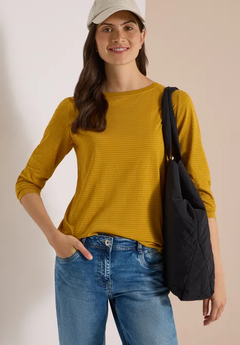Langarm Shirt mit Boat Neck und Streifen golden honey Junge Frau in gelbem Langarmshirt, Jeans, Baseballcap und schwarzer Umhängetasche lächelt.