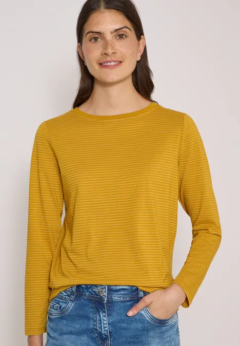 Langarm Shirt mit Boat Neck und Streifen golden honey Frau in gelbem, fein gestreiftem Langarmshirt und Jeans, lächelnd vor hellem Hintergrund.