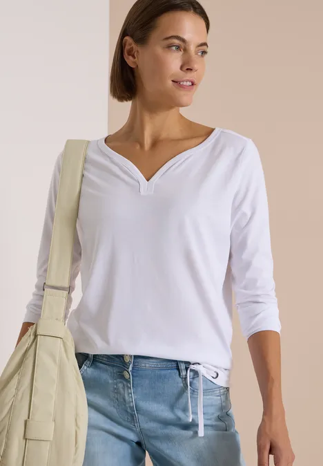 Shirt mit Split Neck im Tunika-Look White Eine Frau trägt eine weiße 3/4-Arm-Bluse, blaue Jeans und eine cremefarbene Umhängetasche vor hellem Hintergrund.