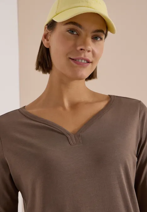 Shirt mit Split Neck im Tunika-Look urban taupe Frau in braunem V-Ausschnitt-Oberteil und gelber Baseballmütze lächelt leicht.