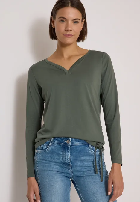 Shirt mit Split Neck im Tunika-Look dried olive green Frau trägt khakigrünes Langarm-Shirt mit V-Ausschnitt und helle Jeans mit seitlicher Schleife.